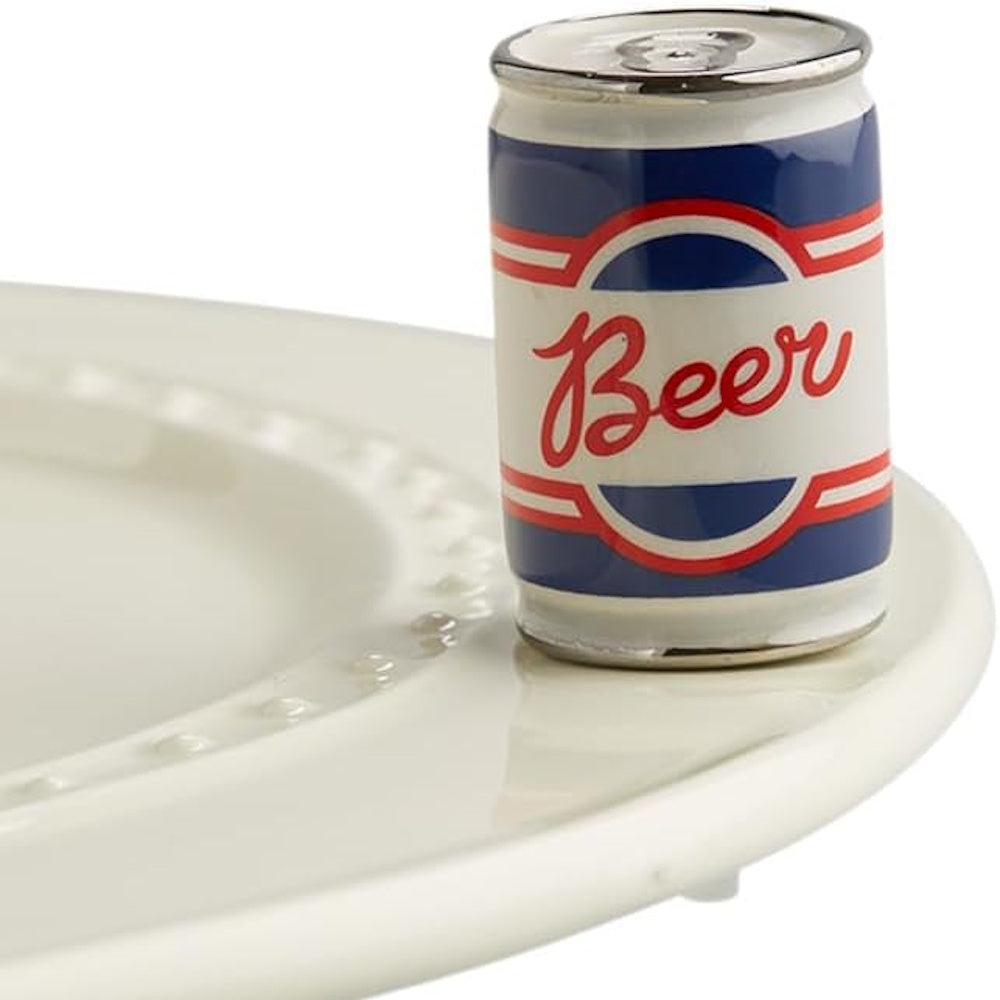 A miniature ceramic beer can figurine sitting on the rim of a white beaded plate.
