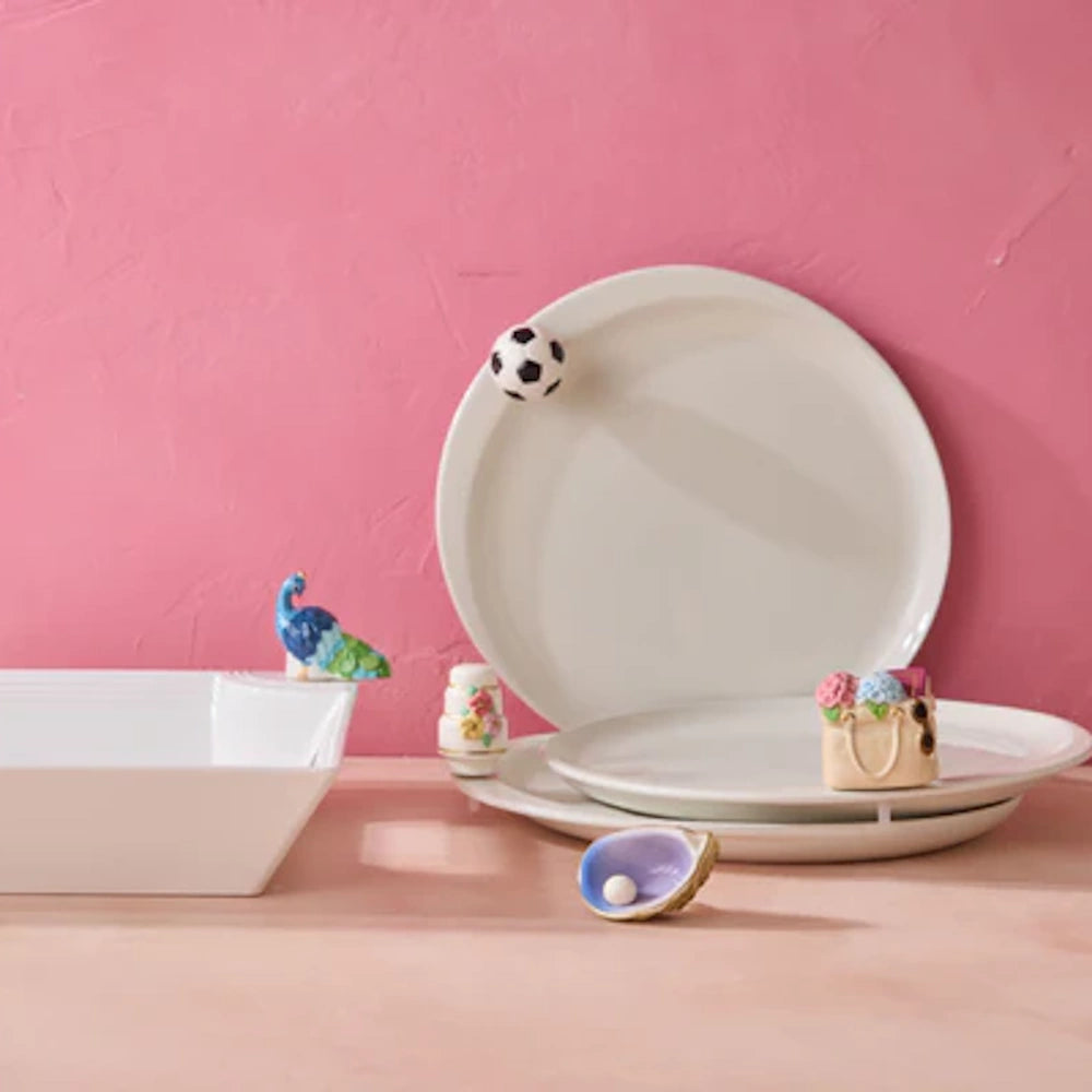 White ceramic plates and bowl decorated with mini charms, including a soccer ball, peacock, and floral tote.