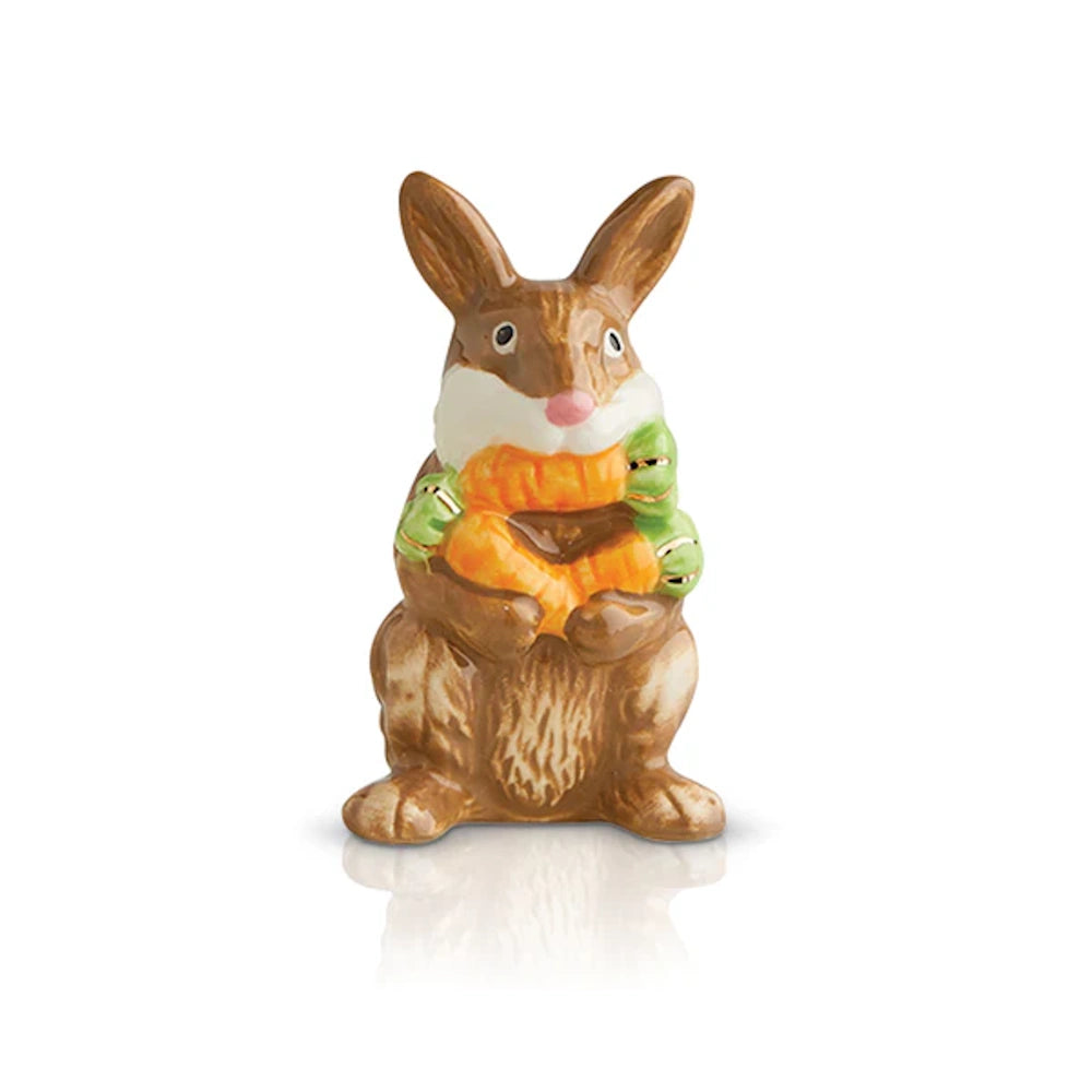 Brown ceramic bunny figurine holding two orange carrots with green tops, standing on a white reflective surface.