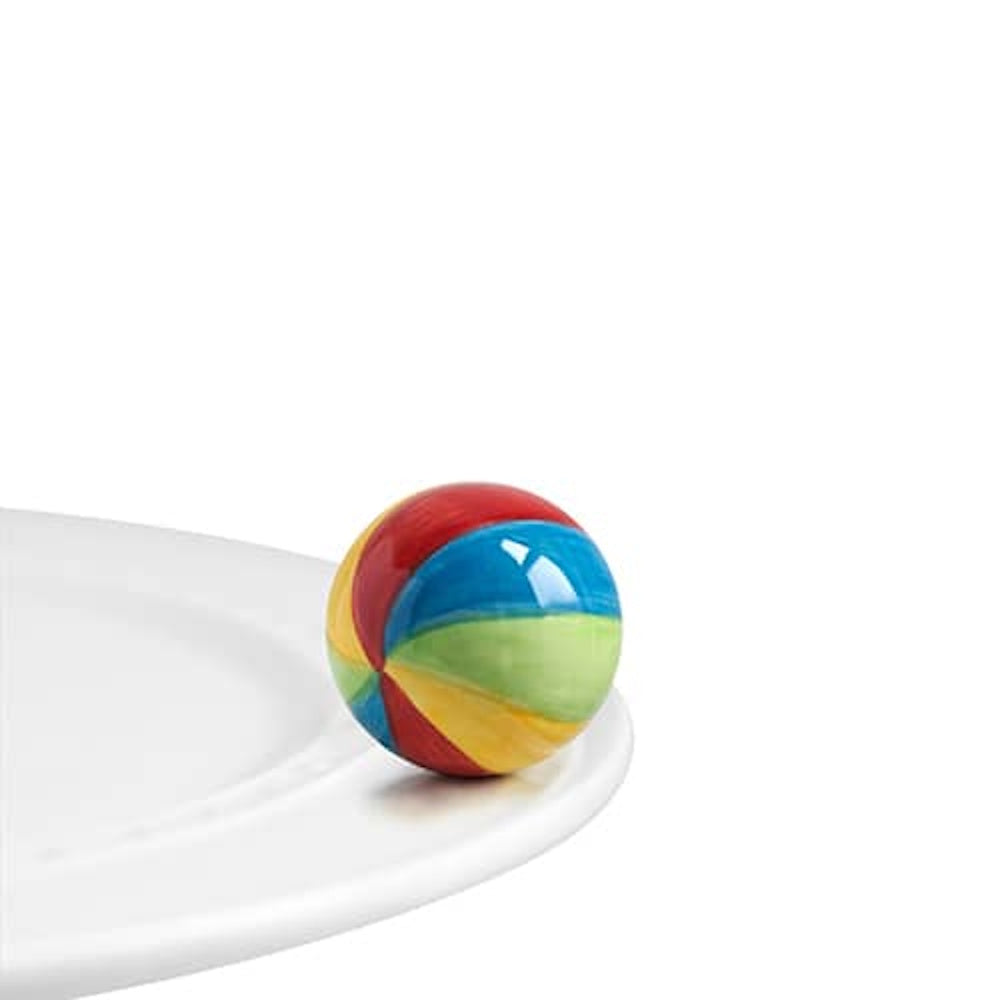 A small, colorful striped beach ball charm attached to the rim of a white ceramic plate.