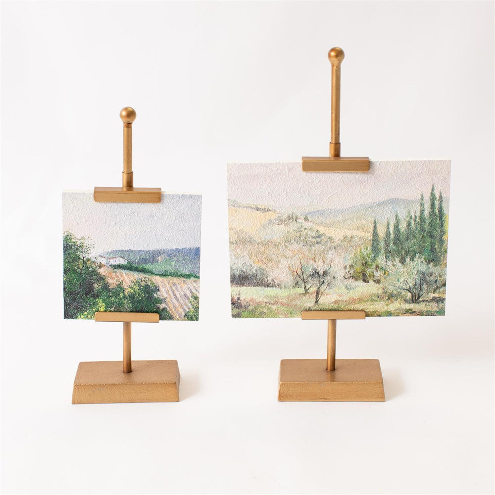 Two mini landscape paintings displayed on elegant gold easel stands against a white background.