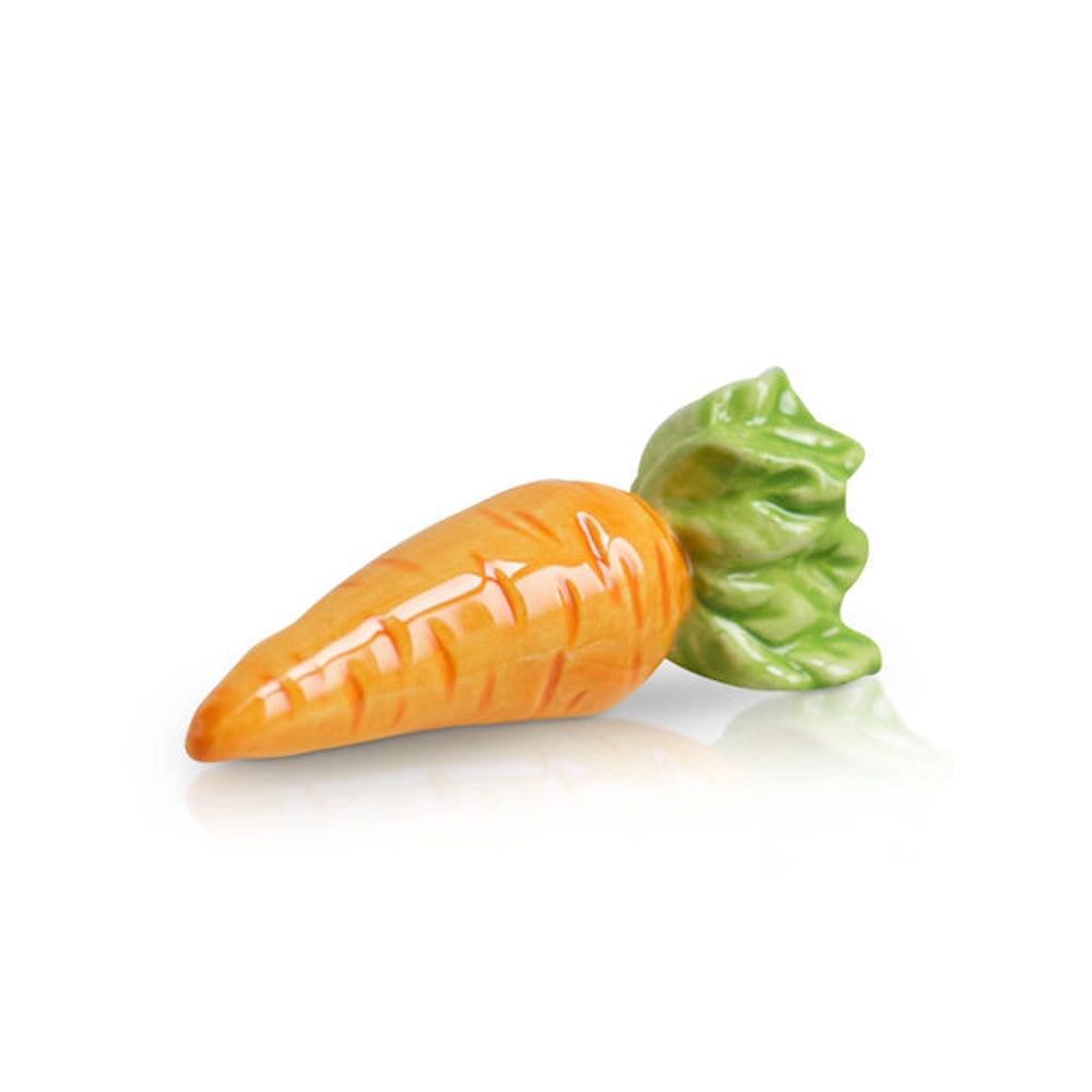 Miniature ceramic carrot figurine with a glossy orange finish and green leafy top on a reflective white surface.