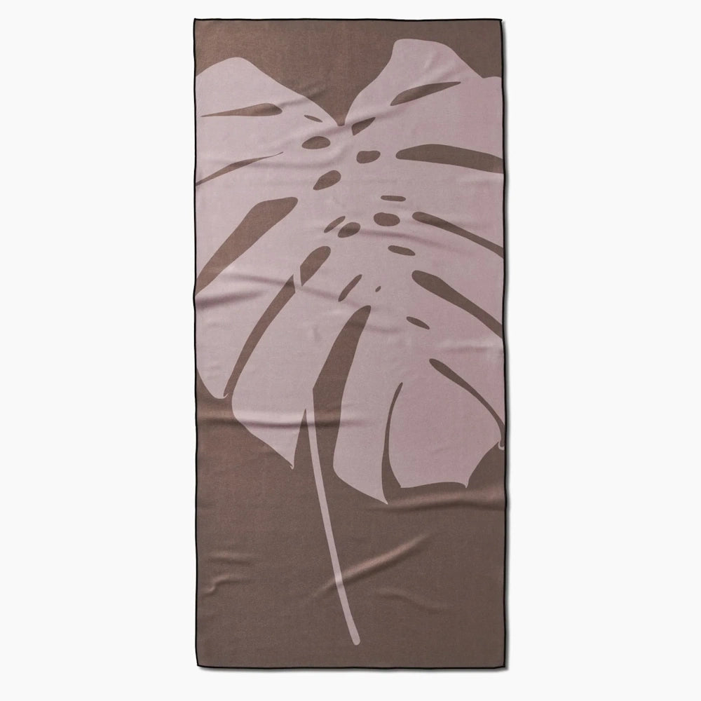 Brown and mauve beach towel featuring a large, stylized monstera leaf graphic against a white background.