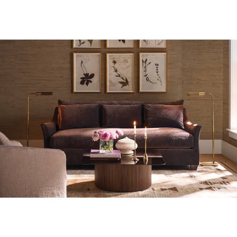 Brown velvet Moreau sofa with a fluted coffee table, gold floor lamps, and botanical wall art.