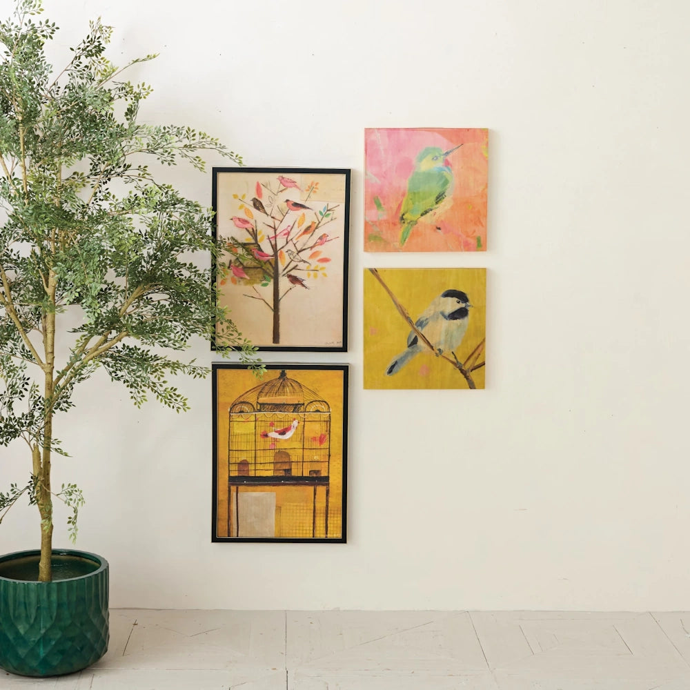 Gallery wall with four bird-themed art pieces in frames, displayed next to a green potted artificial tree on a white wall.