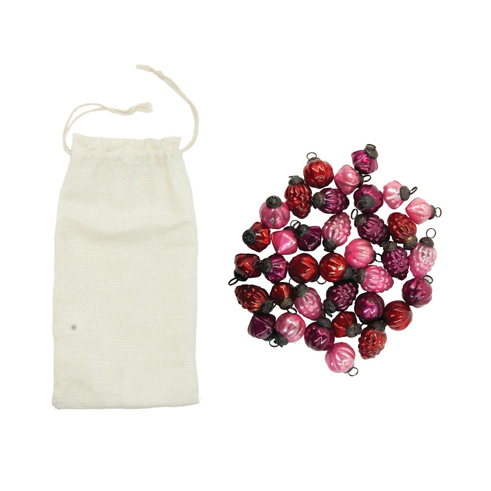 Mini embossed pink and red glass ornaments gathered beside a fabric drawstring pouch.