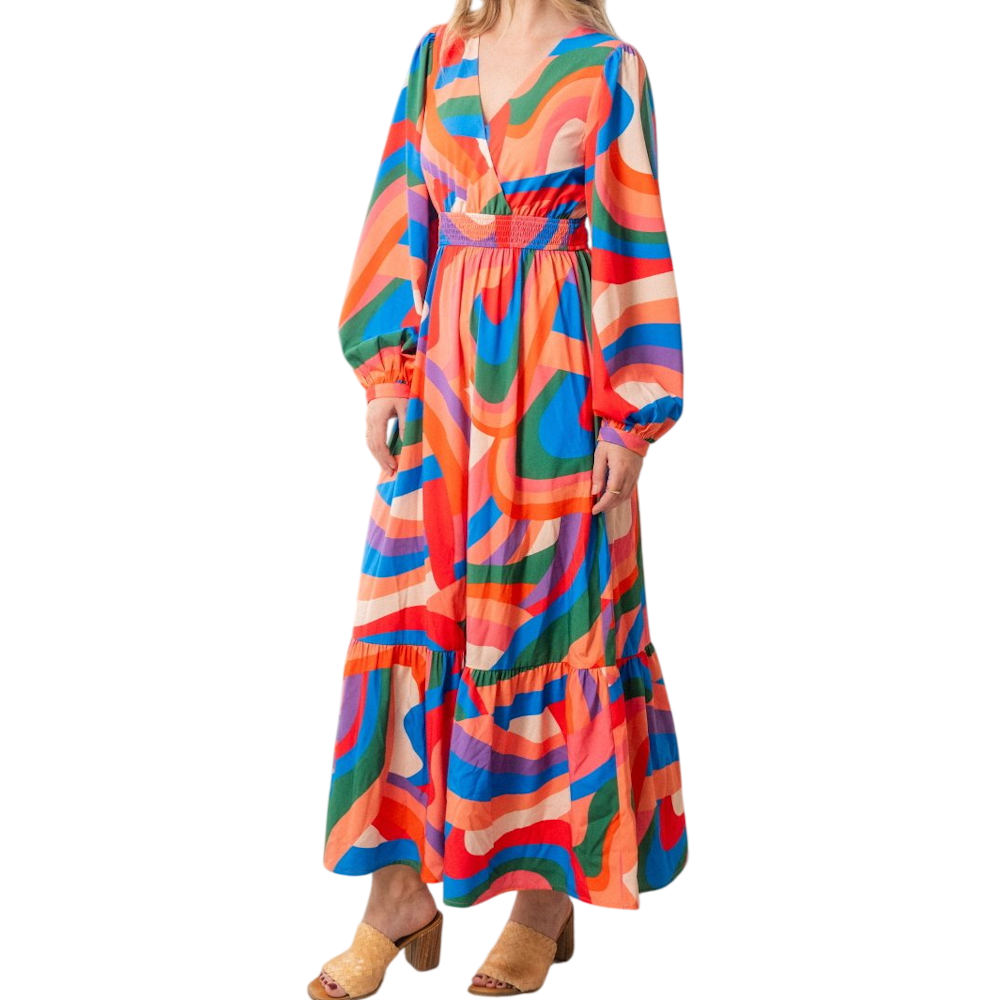 A woman wearing a vibrant, multicolored maxi dress with a retro psychedelic pattern and long sleeves.
