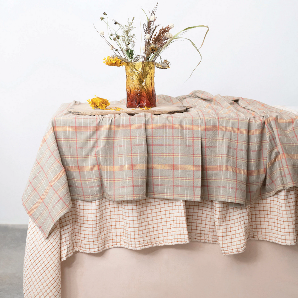 Layered beige plaid tablecloth on a styled table with a vase of dried yellow flowers.