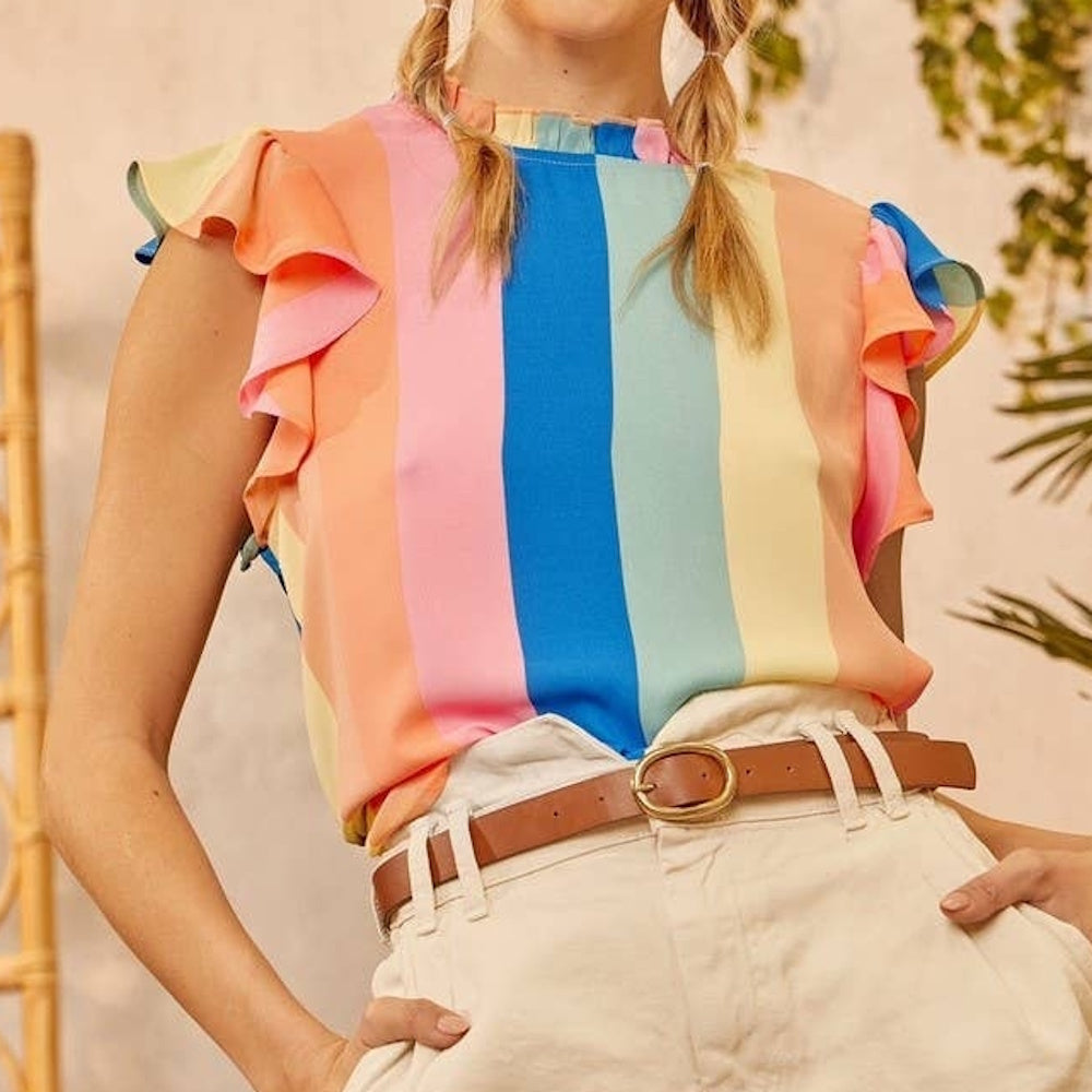 A person wearing a pastel rainbow striped top with ruffle sleeves, tucked into white pants with a brown belt.