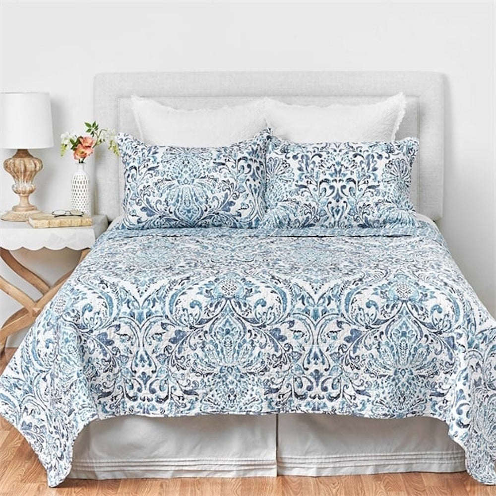 Blue and white damask quilt bedding set on a bed with matching pillows and a light grey headboard.