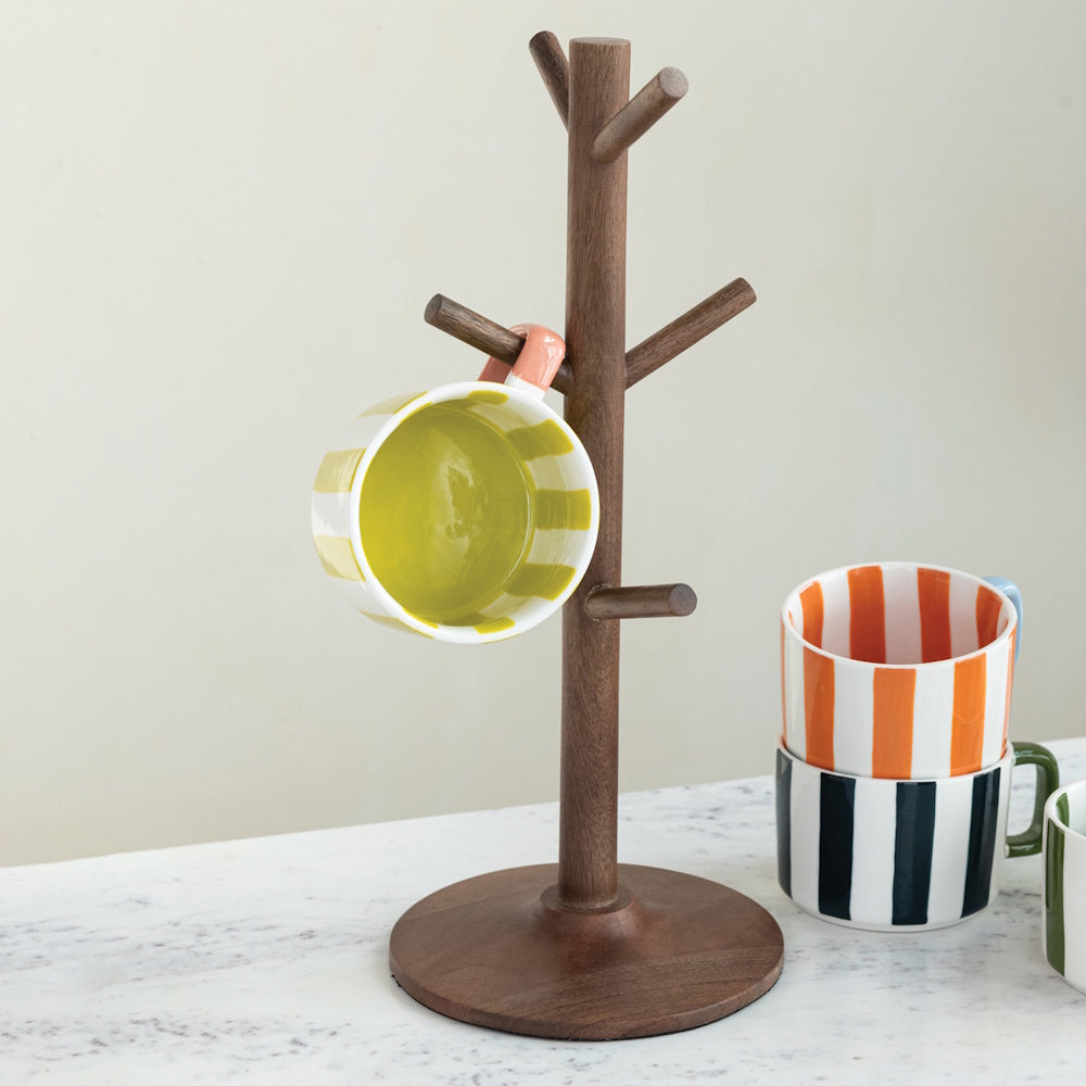 Natural wood mug tree stand holding a striped ceramic coffee cup on a kitchen counter.
