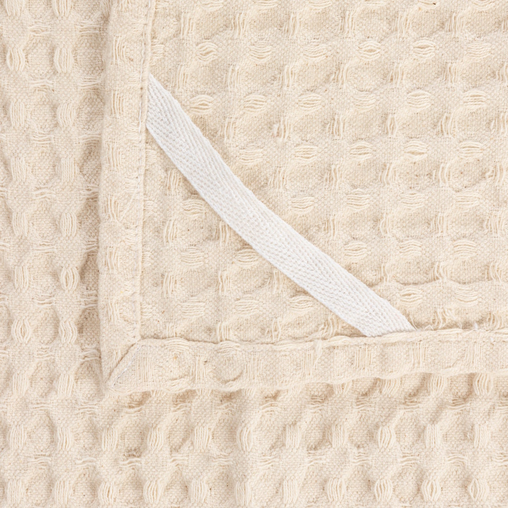 Close-up view of the corner of a natural stonewashed cotton waffle weave tea towel featuring a hanging loop.
