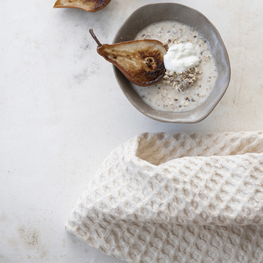 Natural stonewashed cotton waffle weave tea towel displayed with a bowl of oatmeal topped with a roasted pear and yogurt.