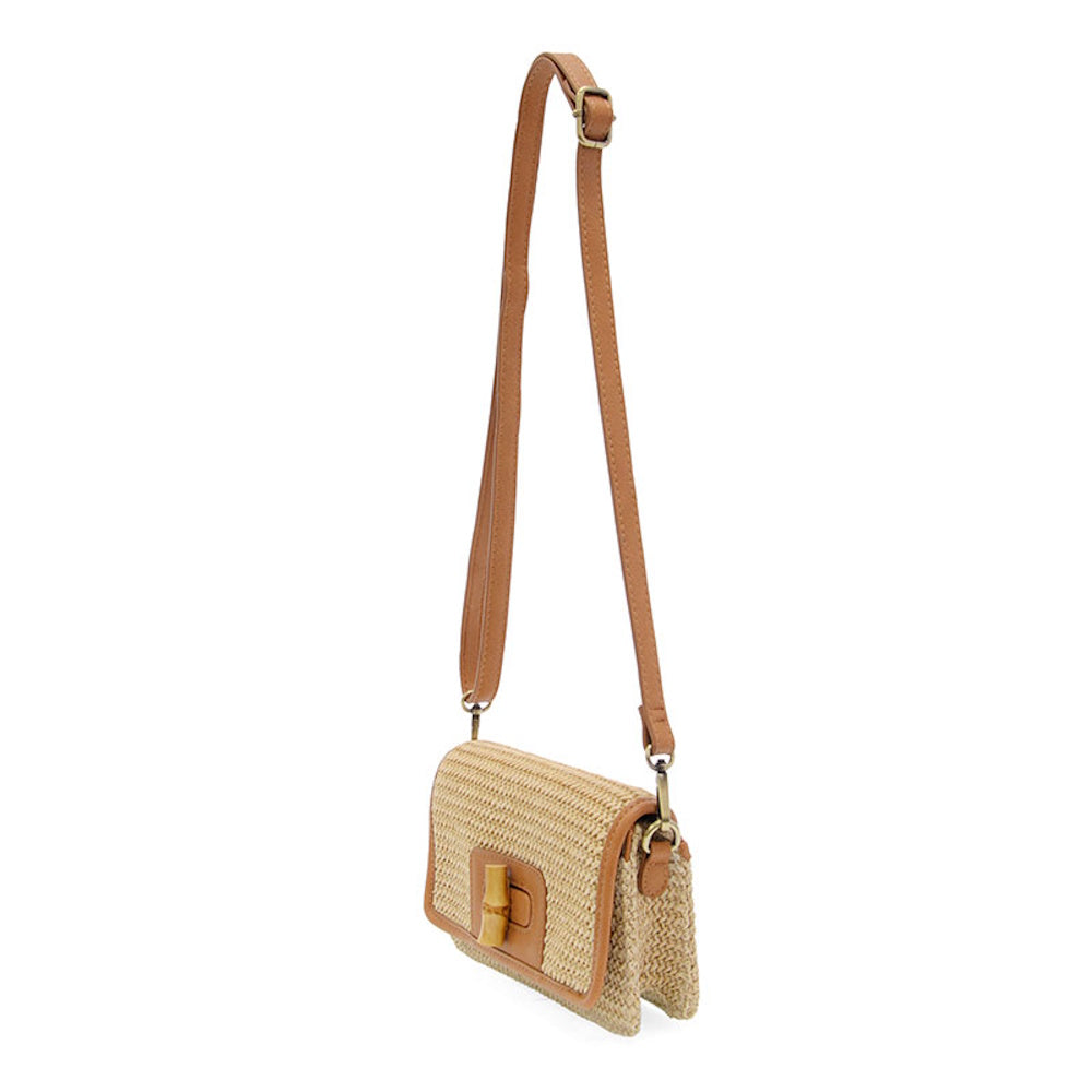 Woven straw crossbody bag with tan leather trim, long shoulder strap, and a natural bamboo turnlock closure on the front.