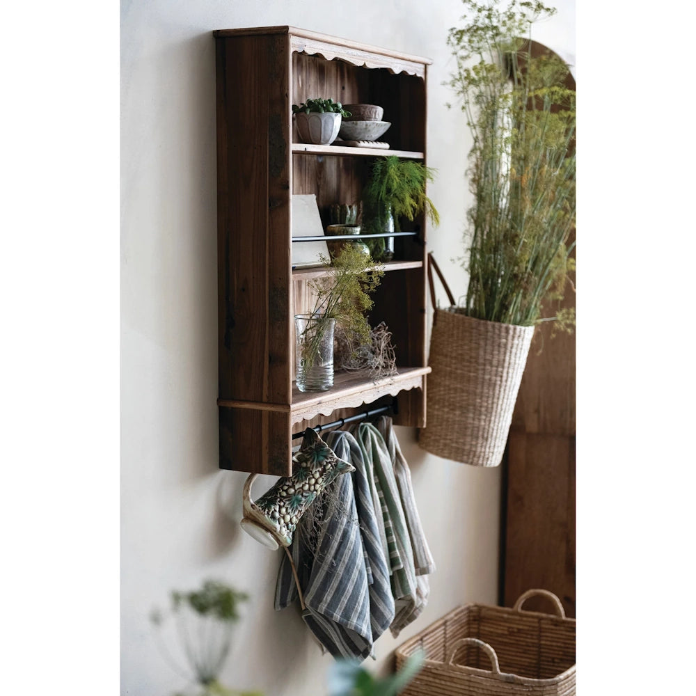 Rustic natural wood wall shelf with scalloped edges, holding plants and decor above hanging striped linens.