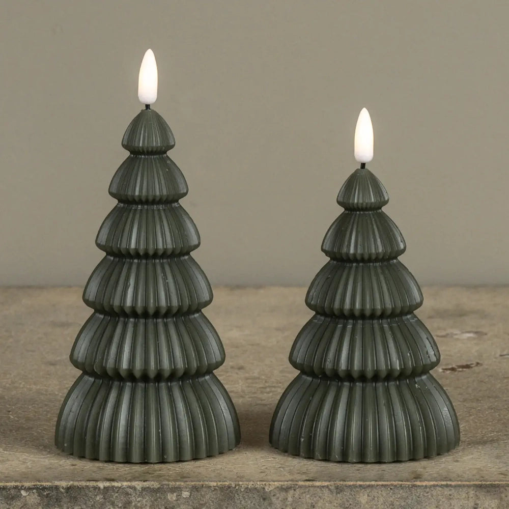 Two dark green tree-shaped flameless candles with lit faux flames on a rustic surface.