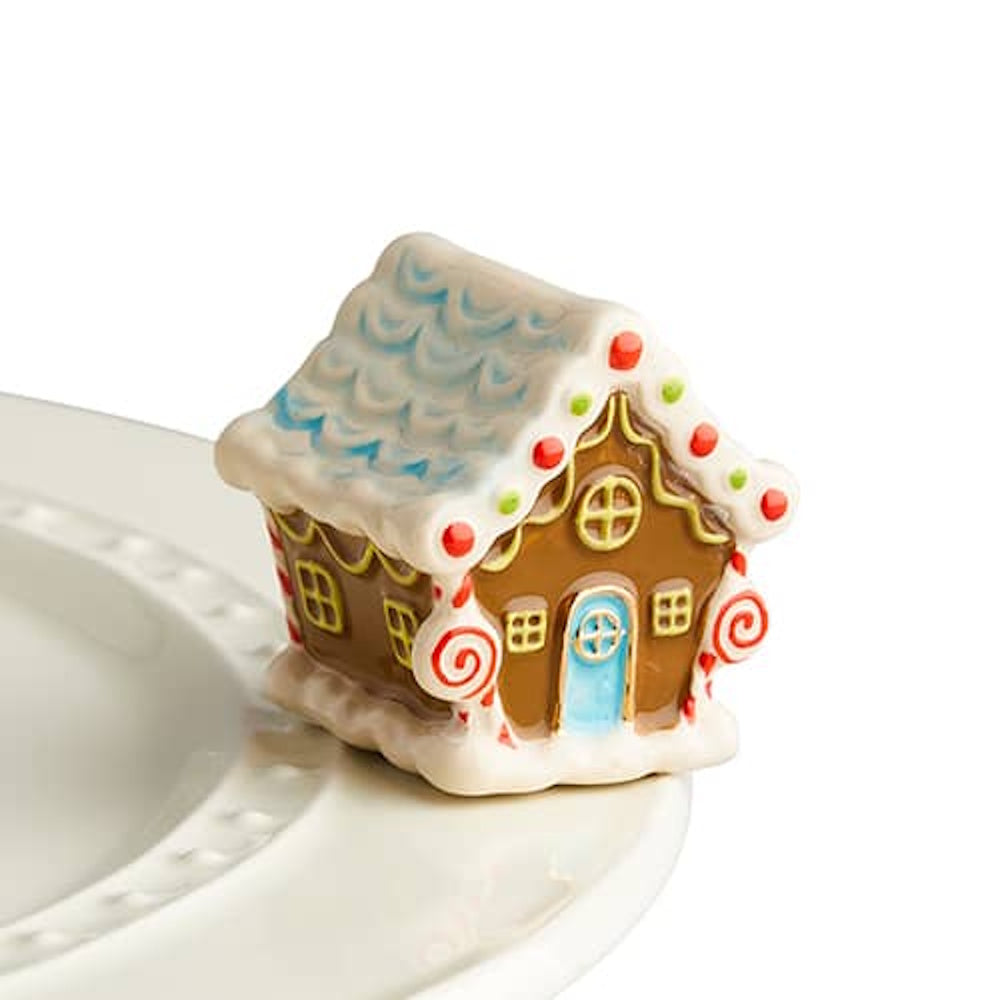A ceramic gingerbread house figurine with white icing, peppermint swirls, and a blue door on a plate rim.