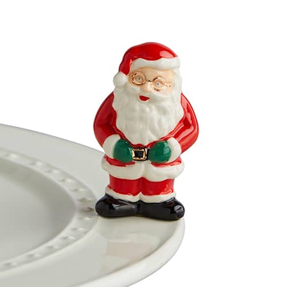 Ceramic Santa Claus figurine with a white beard and green mittens on the rim of a white plate.