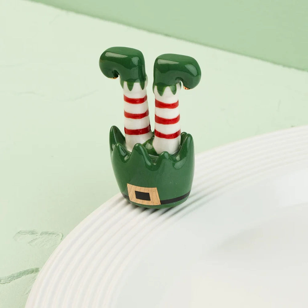 A ceramic elf legs figurine with red and white striped socks on a white plate rim against a green background.