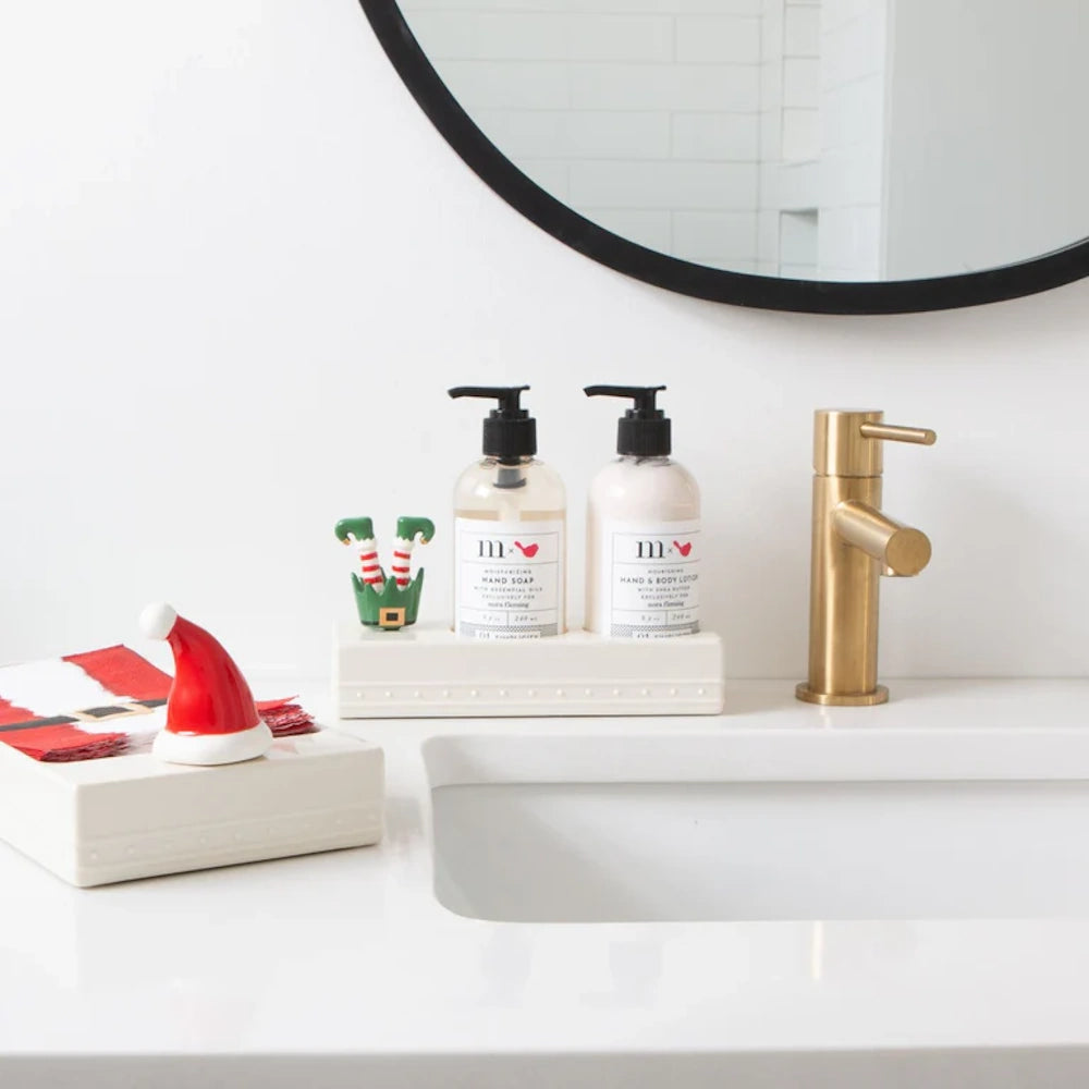 Christmas-themed ceramic charms decorate a modern bathroom counter next to soap dispensers and a gold faucet.