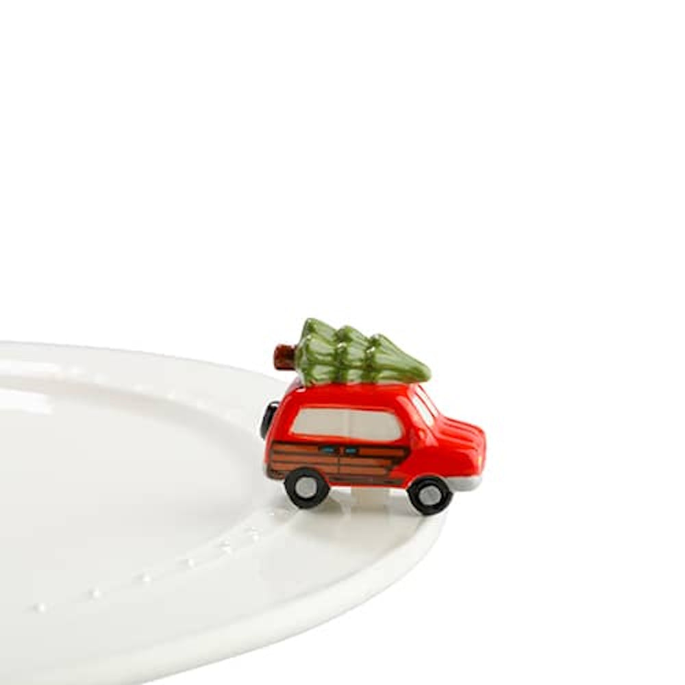 Ceramic red station wagon charm with a green Christmas tree on top, attached to the rim of a white platter.