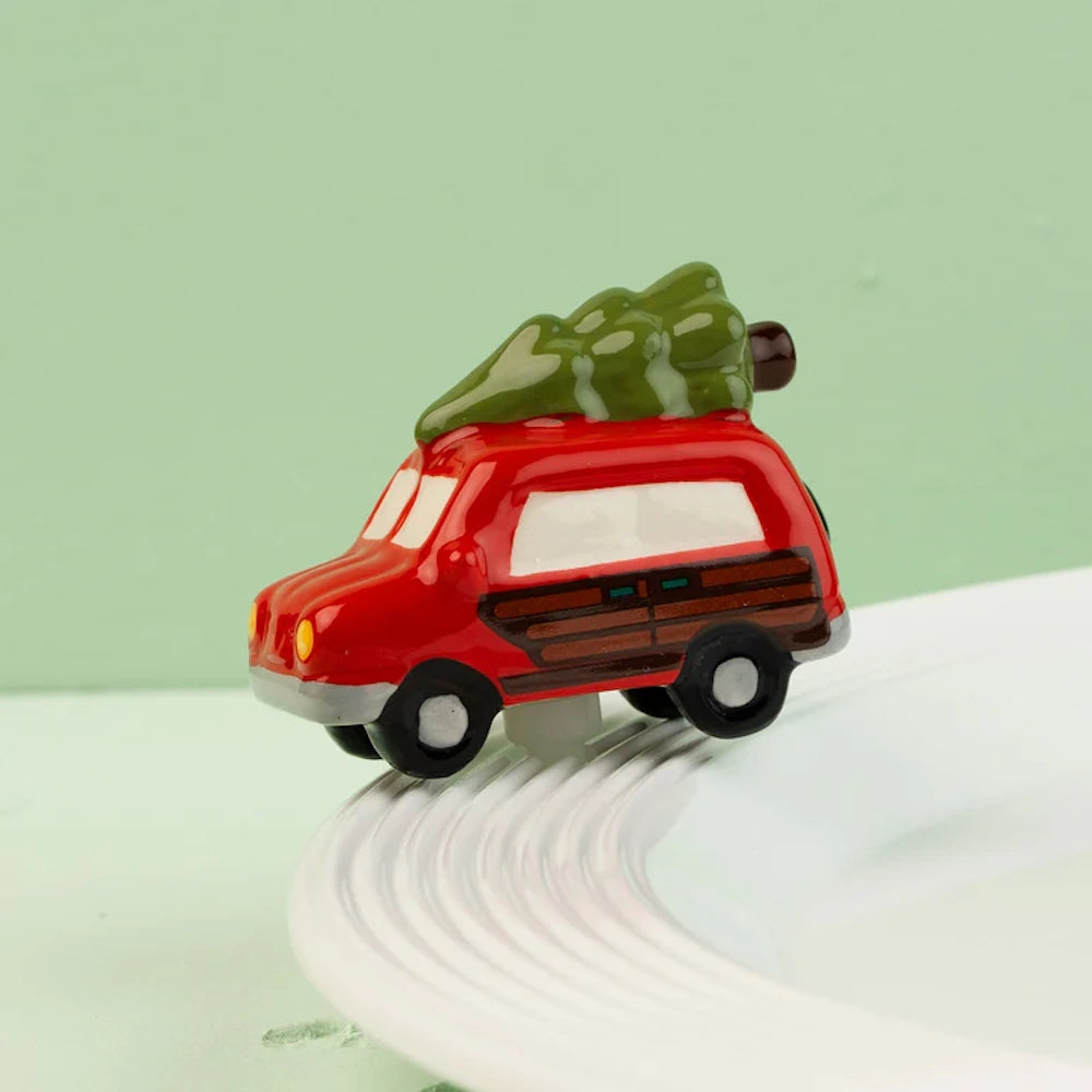 A ceramic station wagon charm with a Christmas tree on its roof rests on the rim of a white dish.