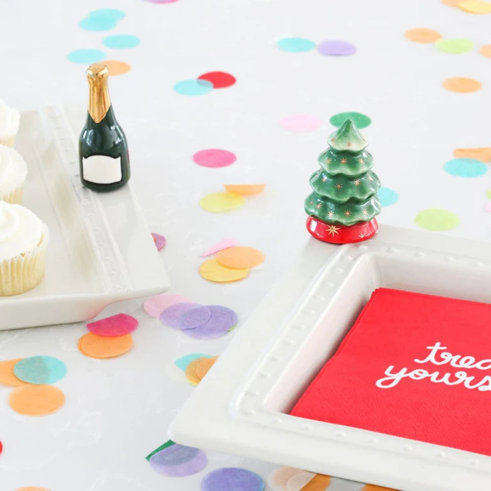 Two white serving trays decorated with a tiny champagne bottle and a miniature green Christmas tree.