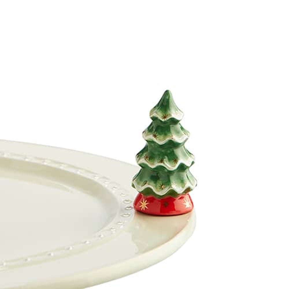 A small ceramic Christmas tree figurine with a red base and gold stars, sitting on the edge of a white plate.