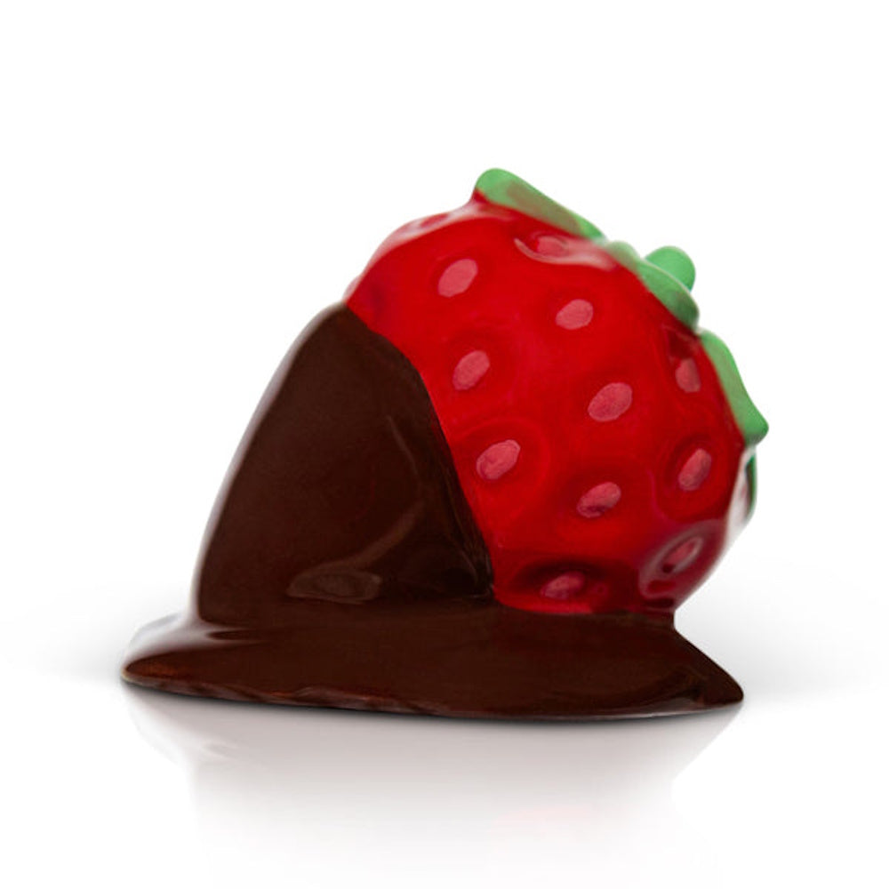 A miniature ceramic figurine of a red strawberry half-dipped in dark chocolate against a white background.