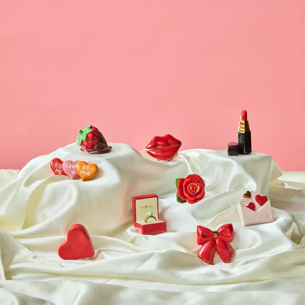 An assortment of Valentine's Day ceramic figurines arranged on a draped white satin fabric.
