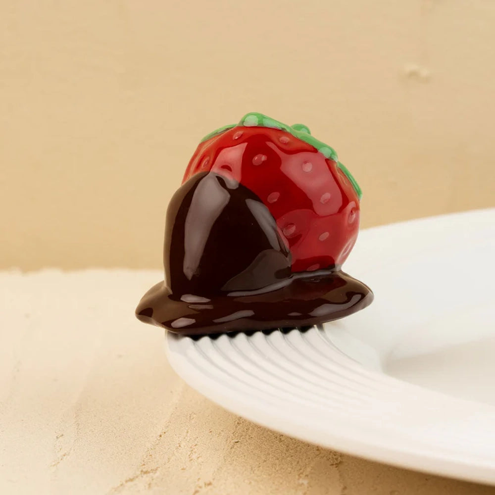 Ceramic chocolate-dipped strawberry figurine resting on the edge of a white ribbed plate.