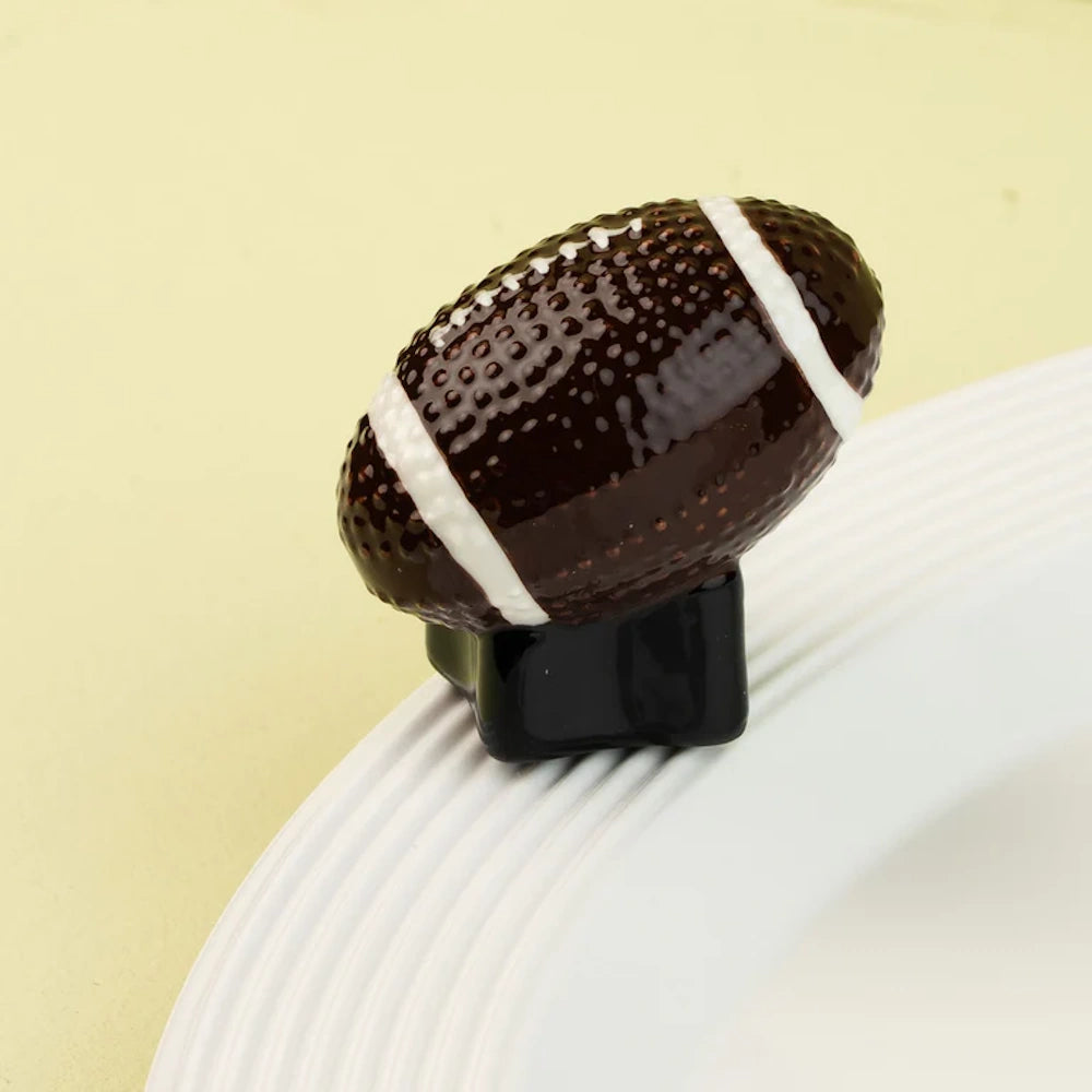 Ceramic brown football figurine with white laces and stripes, resting on the rim of a white plate.