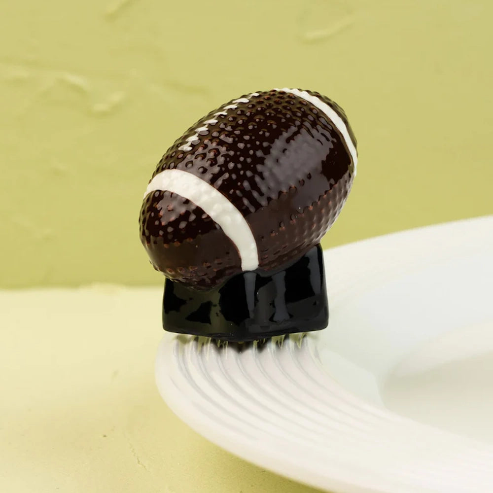 Ceramic textured football figurine on a black base, resting on the rim of a white ribbed plate.