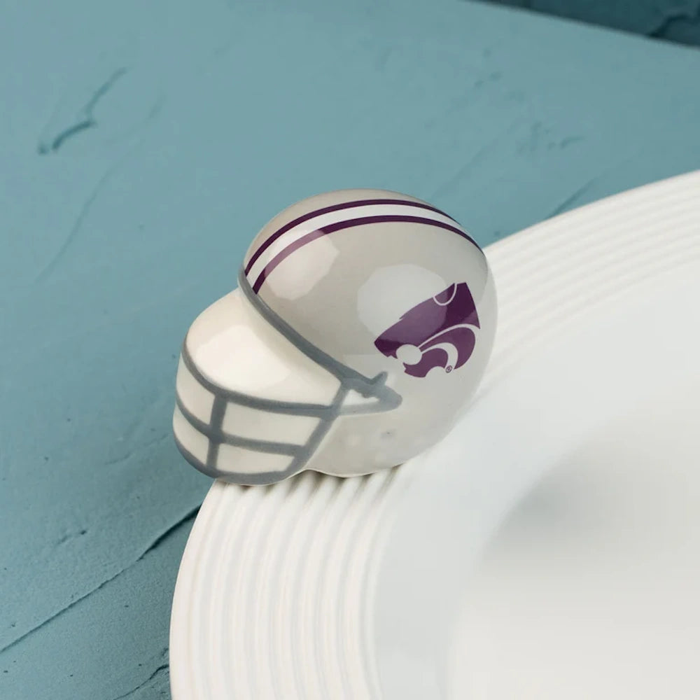 A mini silver football helmet with a grey facemask and purple wildcat logo, resting on a white plate rim.