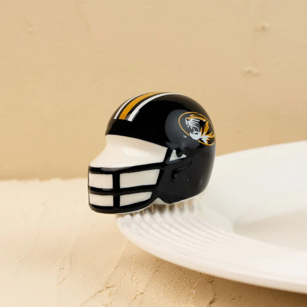A glossy black ceramic football helmet figurine with a tiger logo, perched on the rim of a white plate.