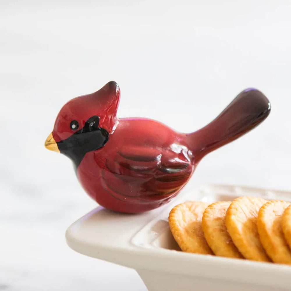 A ceramic red cardinal figurine resting on the corner of a white serving dish filled with crackers.