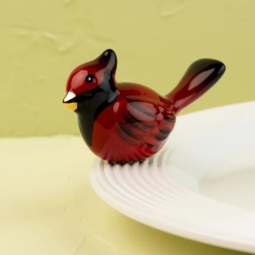 A miniature ceramic red cardinal figurine perched on the rim of a white serving platter.
