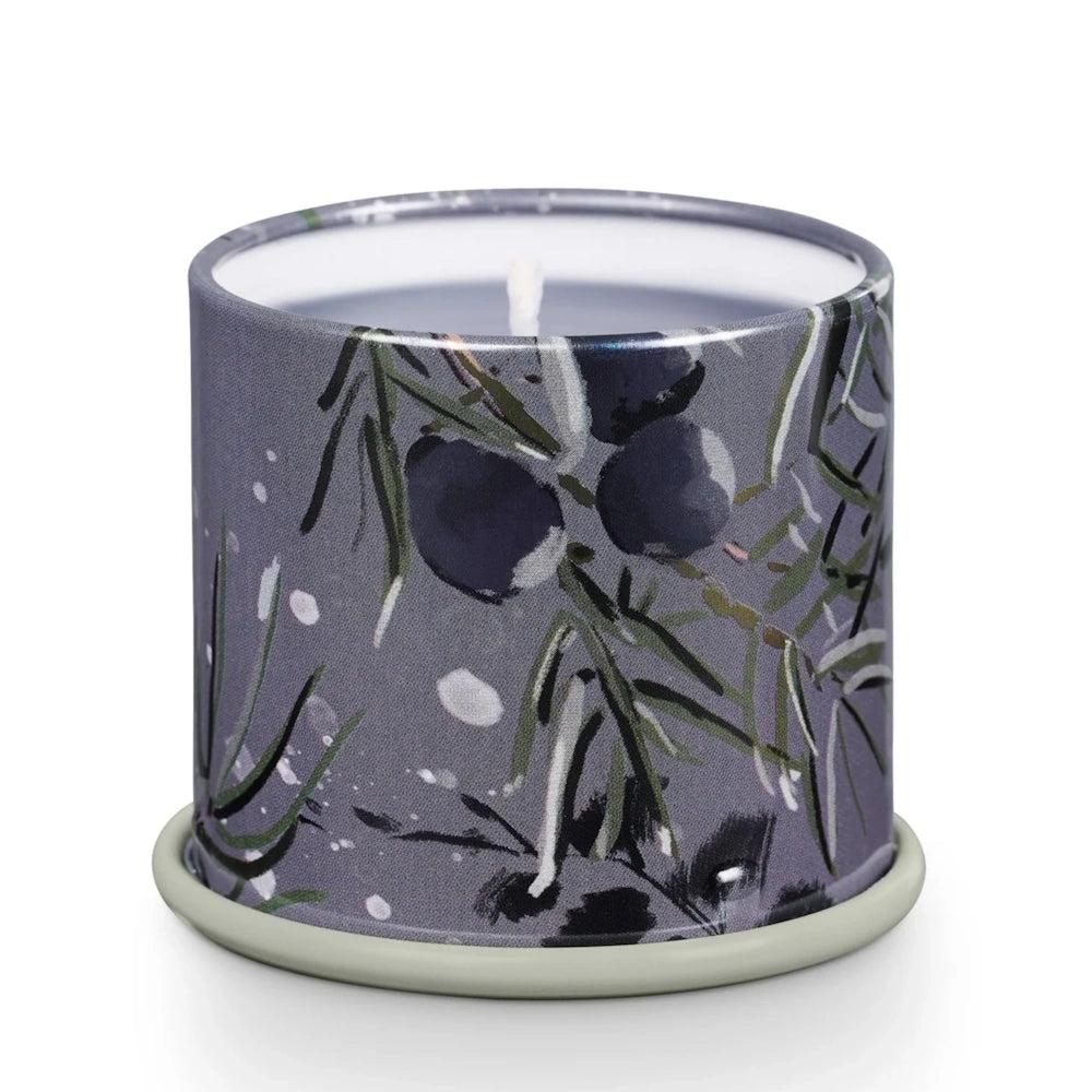 Open tin candle with a white wick, decorated with a dark grey botanical pattern featuring evergreen needles and berries.