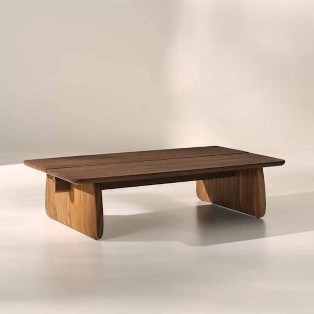 Modern walnut cocktail table styled in a minimalist interior, featuring sculptural panel legs and a rounded rectangular top design.