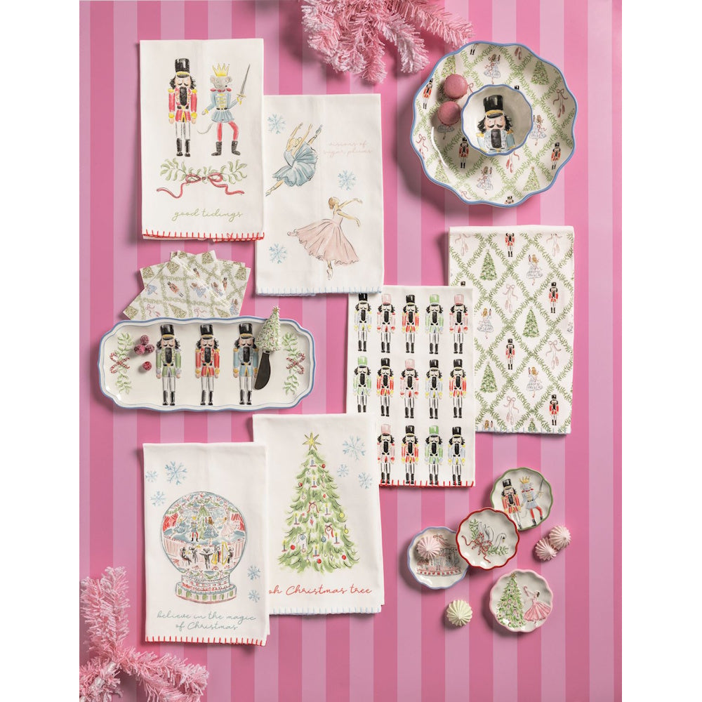 Nutcracker-themed kitchen towels and matching dishware displayed on a pink striped background.