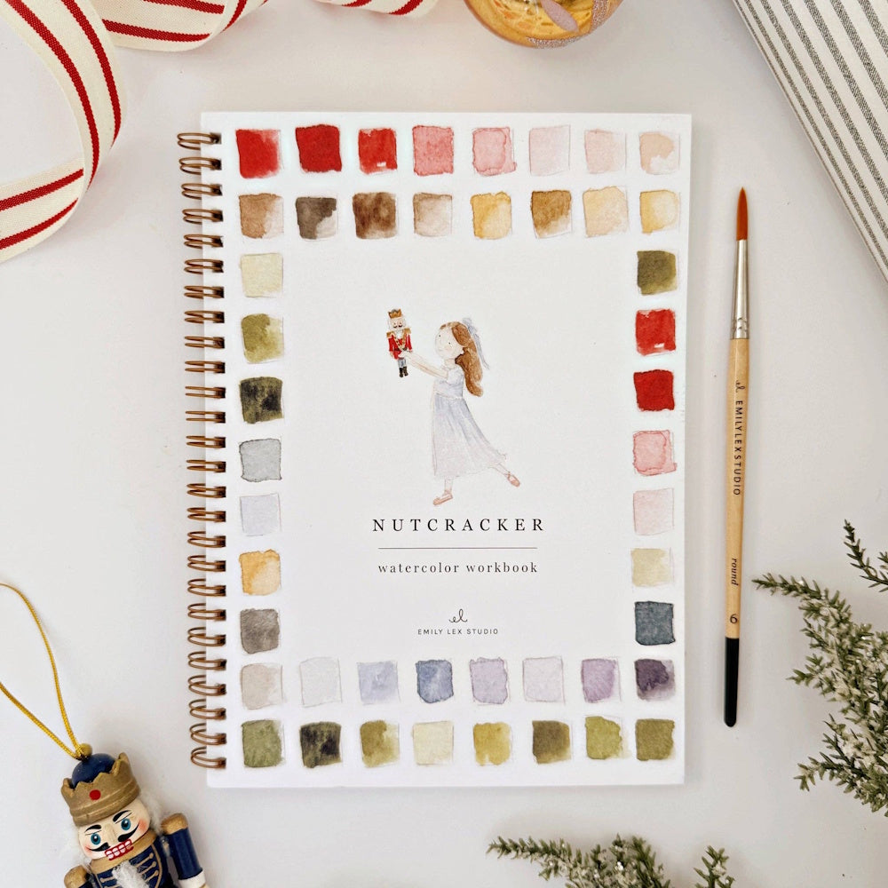 Nutcracker watercolor workbook cover with paint swatches, fine paintbrush, and festive holiday decor.