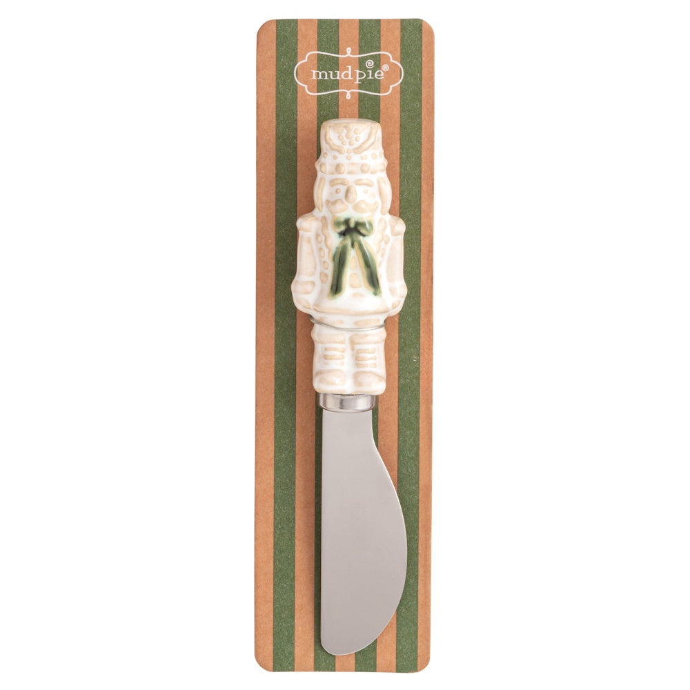 White nutcracker Christmas spreader with a green bow on striped packaging.