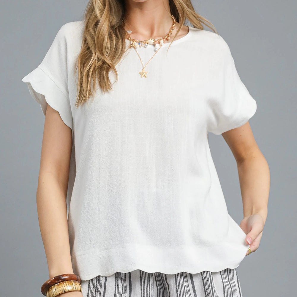 A person wearing a white linen short-sleeve top with ruffled sleeves, necklaces, and striped pants.