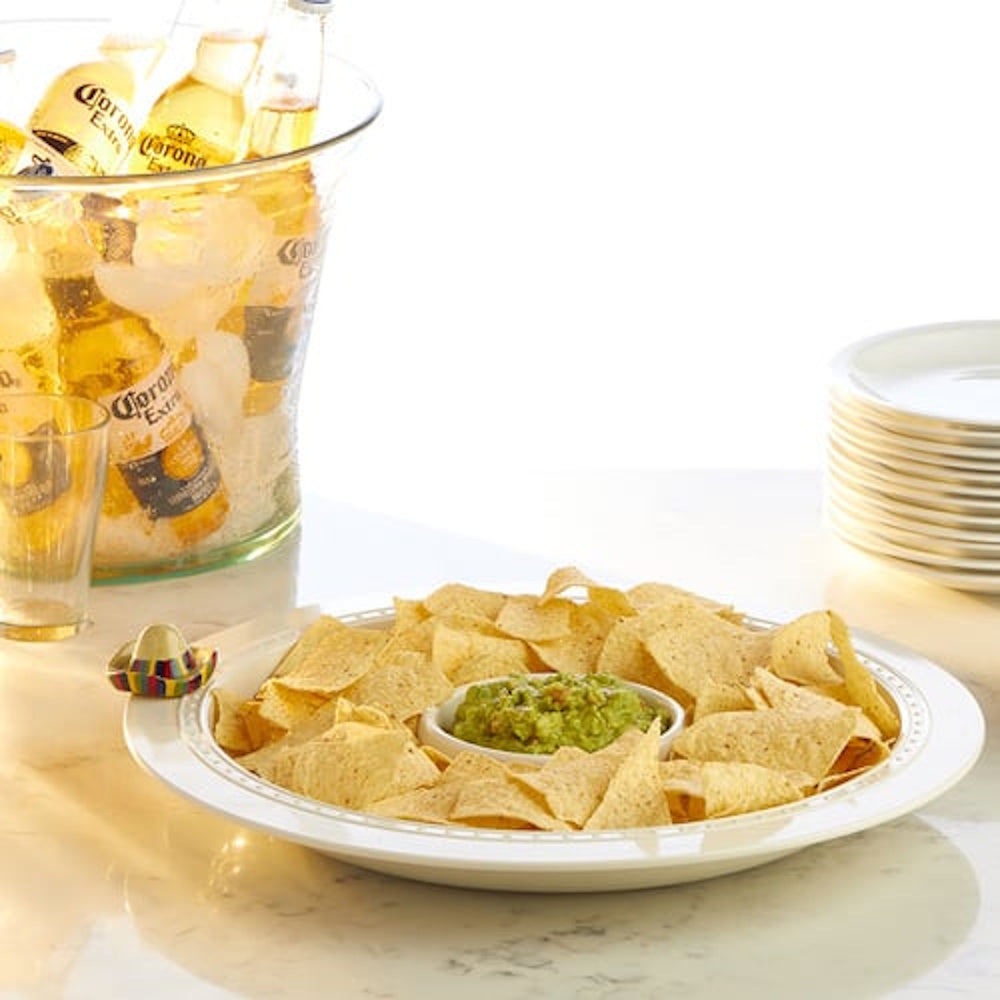 A large platter of tortilla chips and guacamole next to a bucket of iced Corona beers.