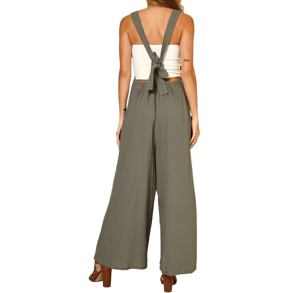 Back view of a woman wearing olive green wide-leg overalls with a tied back over a white tube top.