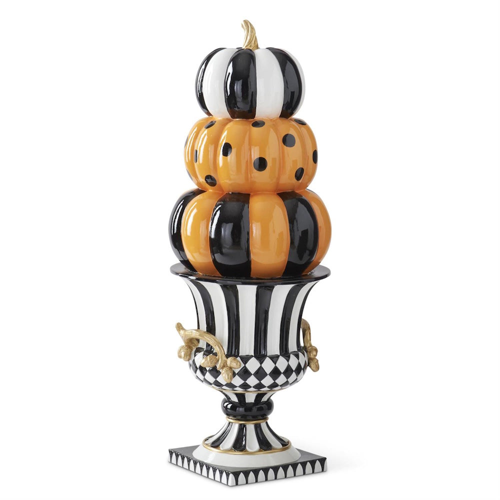 Angled side view of stacked patterned pumpkins in black, white, and orange set atop a decorative urn.