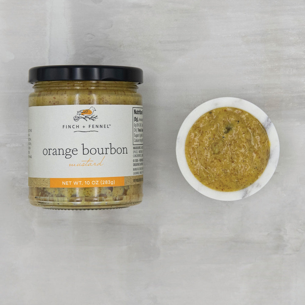 A jar of Finch + Fennel orange bourbon mustard next to a small marble bowl filled with the mustard.