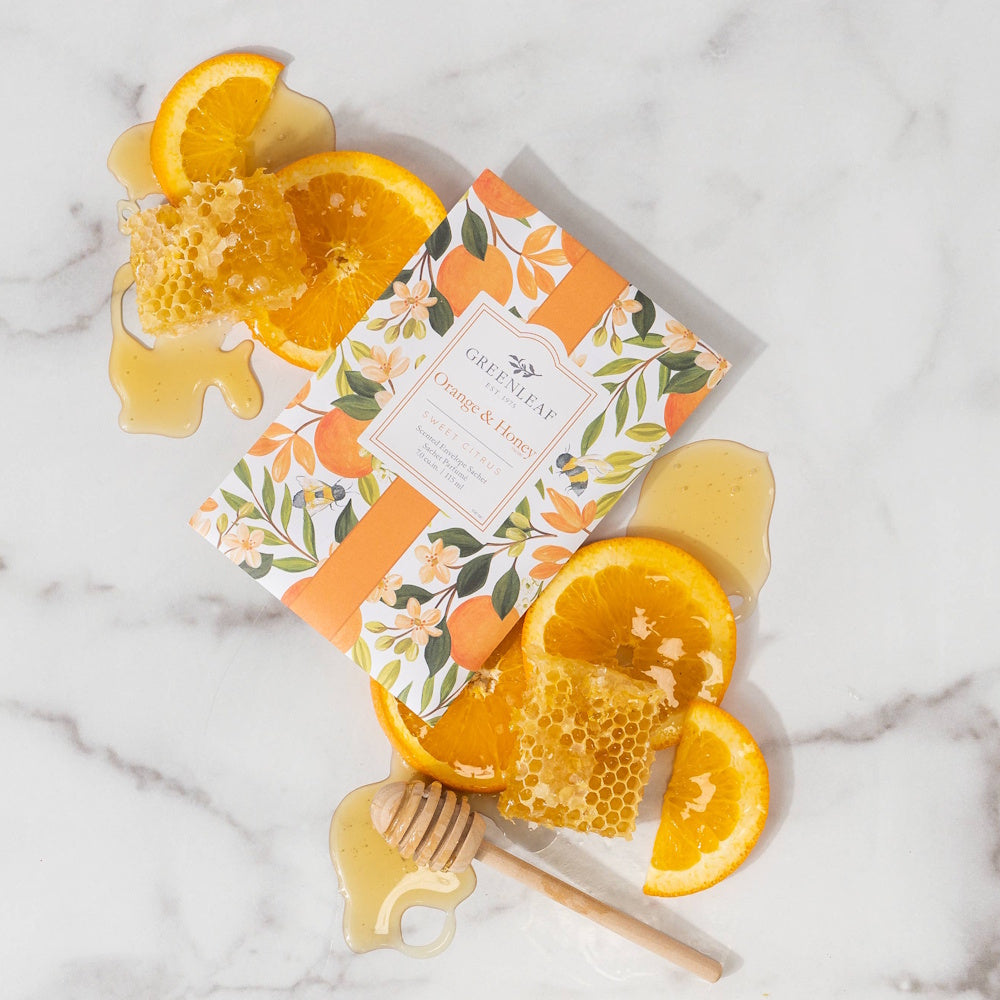 Greenleaf Orange and Honey scented sachet with fresh orange slices, honeycombs, and honey dipper on white marble.