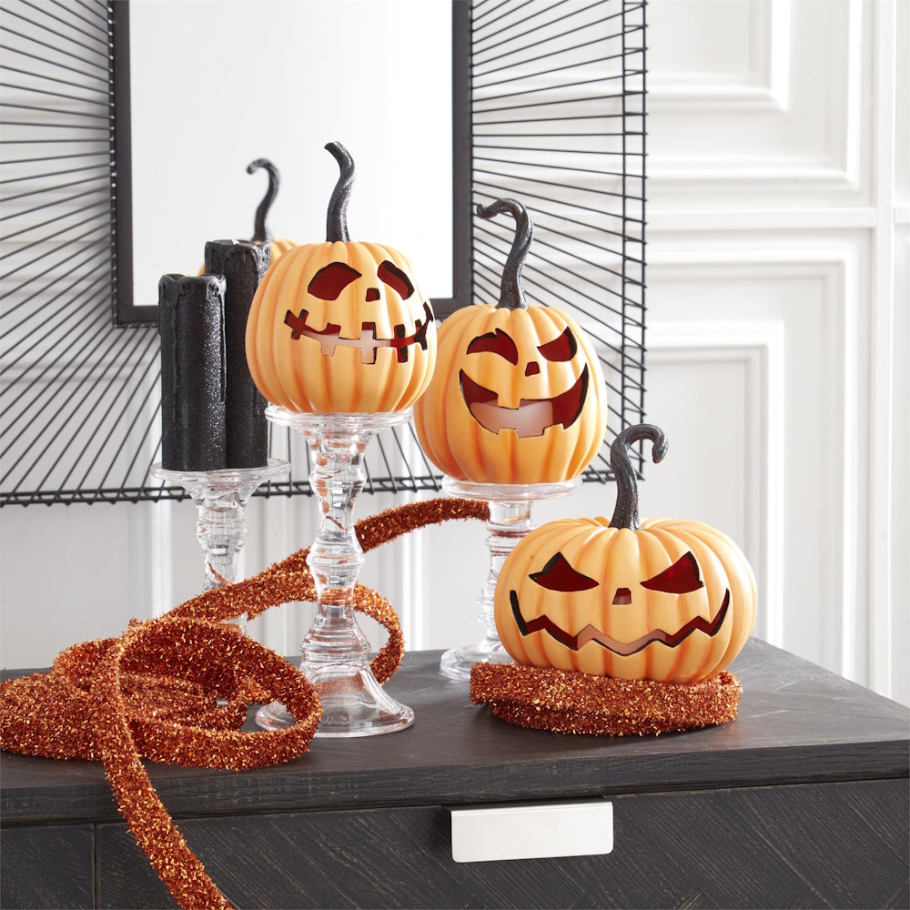 Three resin LED jack-o'-lanterns displayed on glass stands and a table with Halloween tinsel.