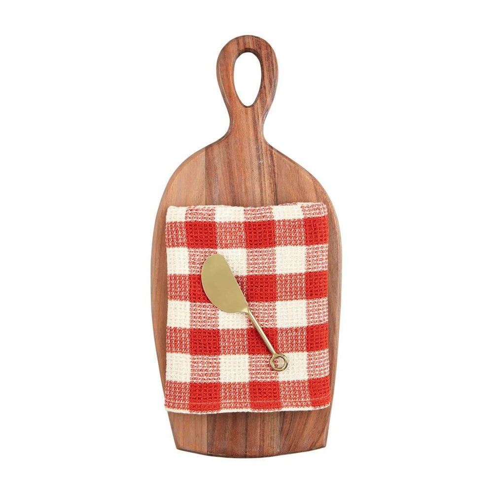 A red and white checkered towel and a gold spreader knife on an oval wooden cutting board with a handle.